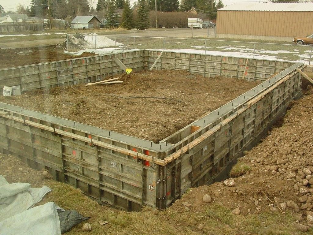 Concrete foundation formwork for a rectangular building, set in a dirt yard.