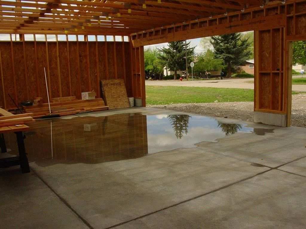Partially built garage with a water-covered concrete floor and unfinished wooden walls.