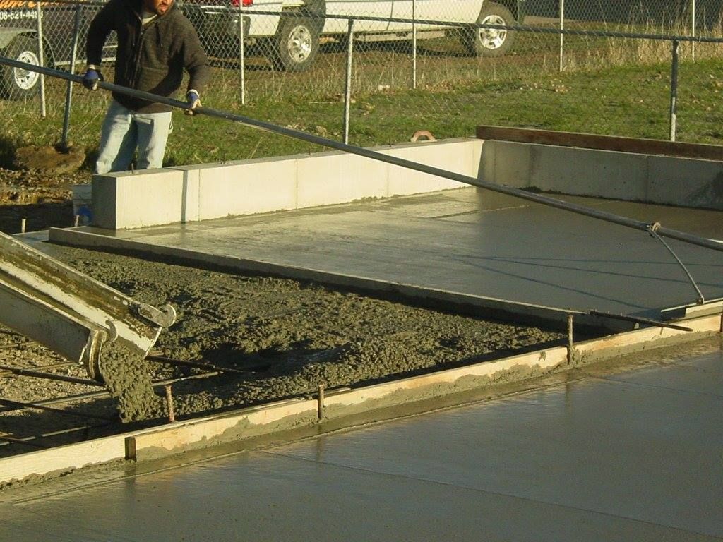 Man leveling wet concrete with a screed; concrete being poured into a form.