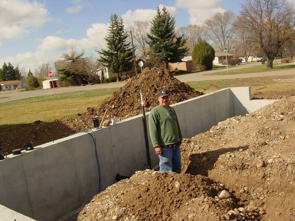 Man stands by a concrete foundation with piles of dirt in a residential area.