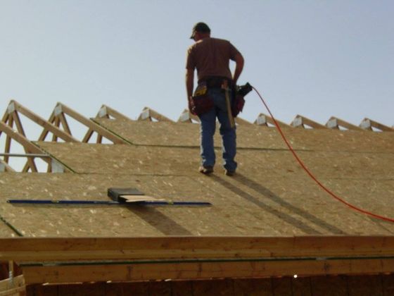 Construction worker on a roof, installing sheathing. Wooden trusses and sky background.
