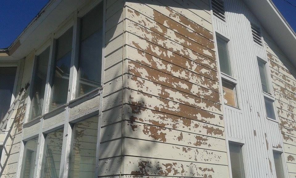 House exterior with peeling paint on siding, multiple windows, and a blue sky.
