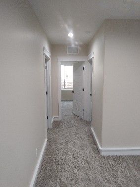 Hallway with beige walls, carpet, and doorways leading to rooms.