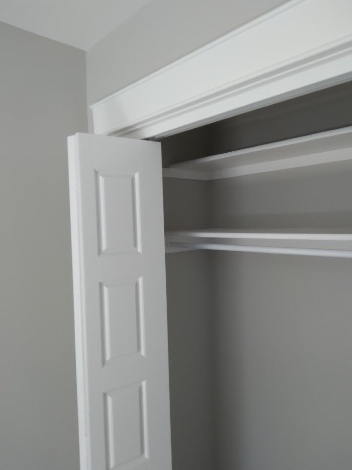 White closet door partially open, revealing shelving inside a gray-walled closet.