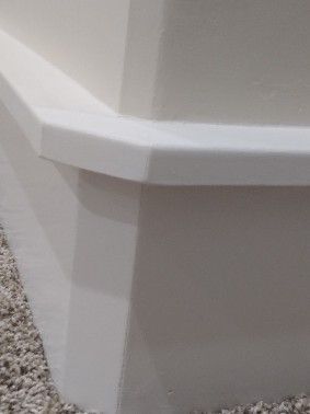 White painted corner molding on a wall and carpeted floor.