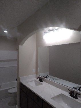Bathroom with double sink vanity, large mirror, and overhead lighting. Beige walls and white countertop.
