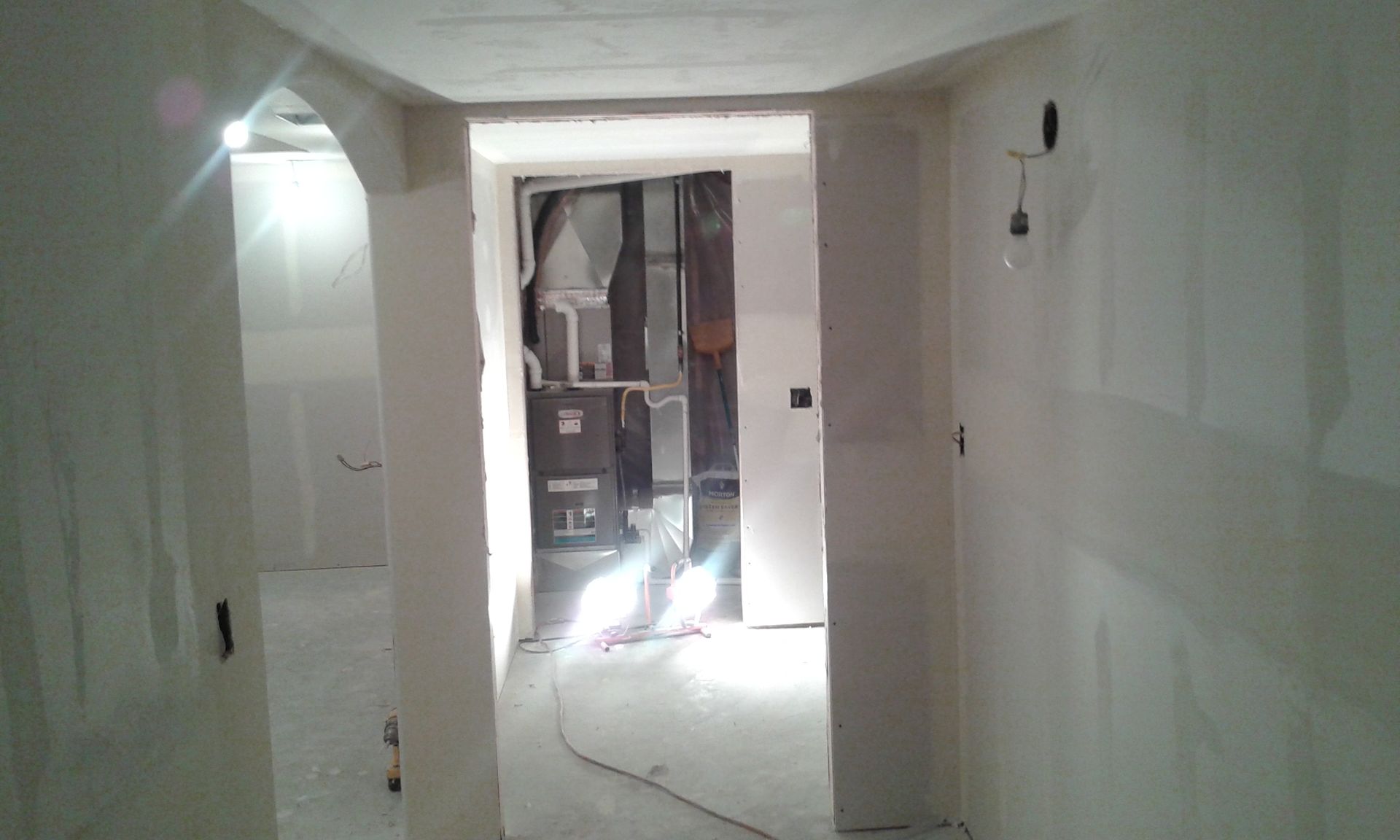 Hallway under construction, drywall walls, door frames, unfinished ceiling, bright light.