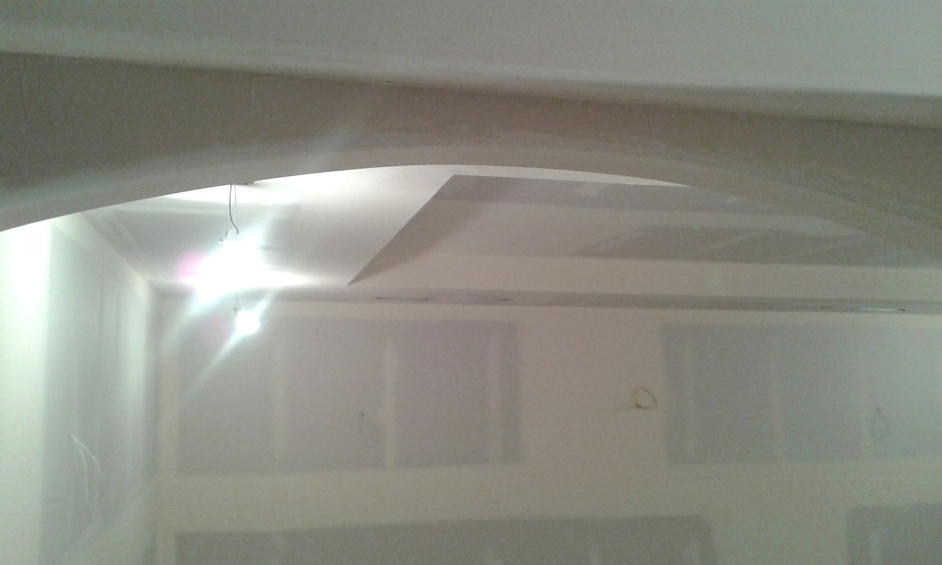 Interior view of a room with drywall on walls and ceiling, including an archway and recessed ceiling feature.