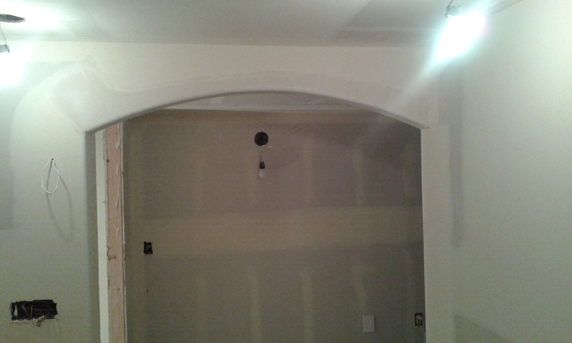 Archway in a room under construction with exposed drywall and electrical fixtures.