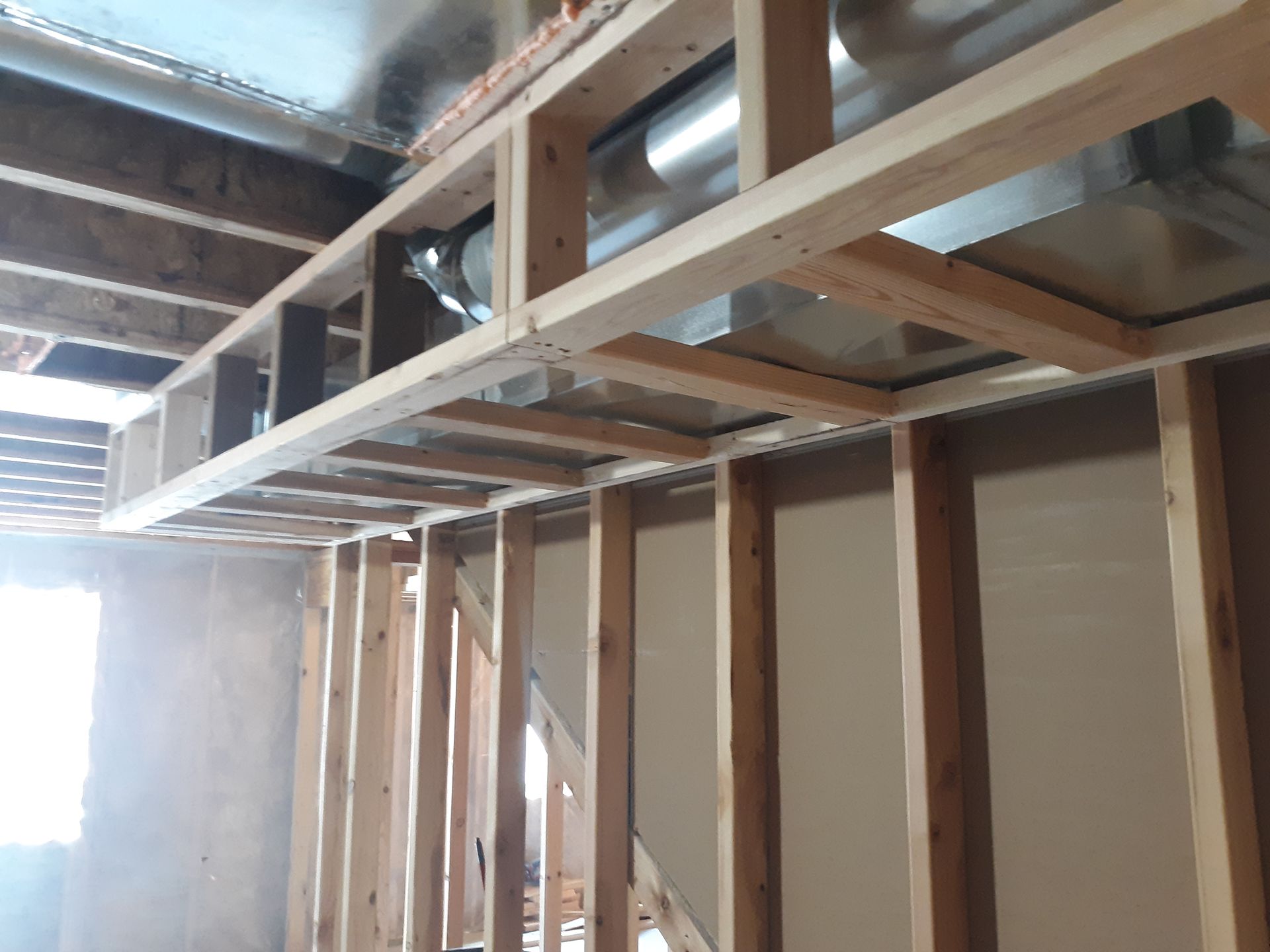 Wooden framing around ductwork in a construction setting; visible studs and unfinished walls.