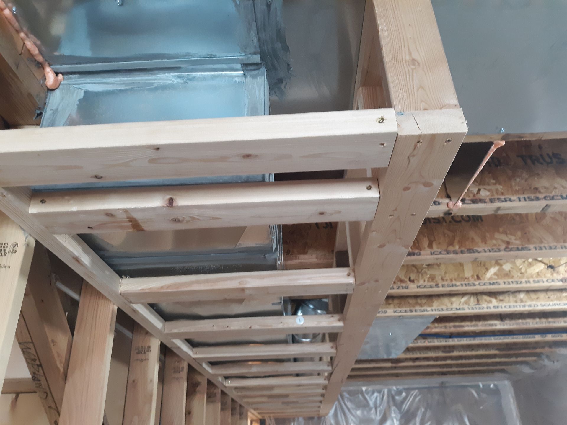 Wooden framing supports HVAC ductwork in a room under construction, with exposed insulation.