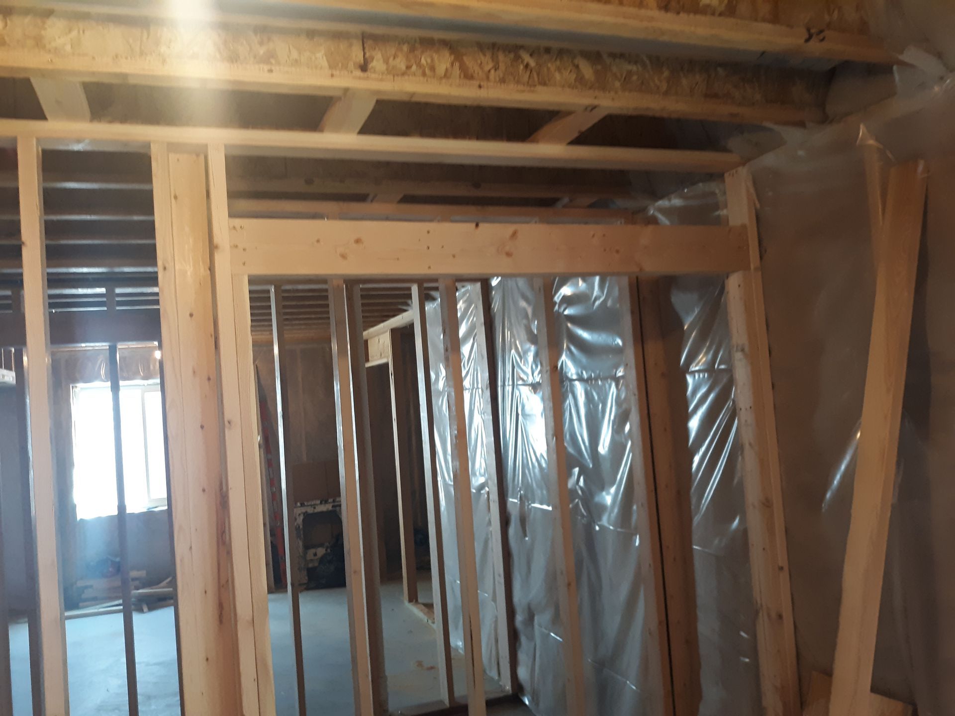 Interior view of wooden framing for a room or doorway under construction, with plastic sheeting on walls.