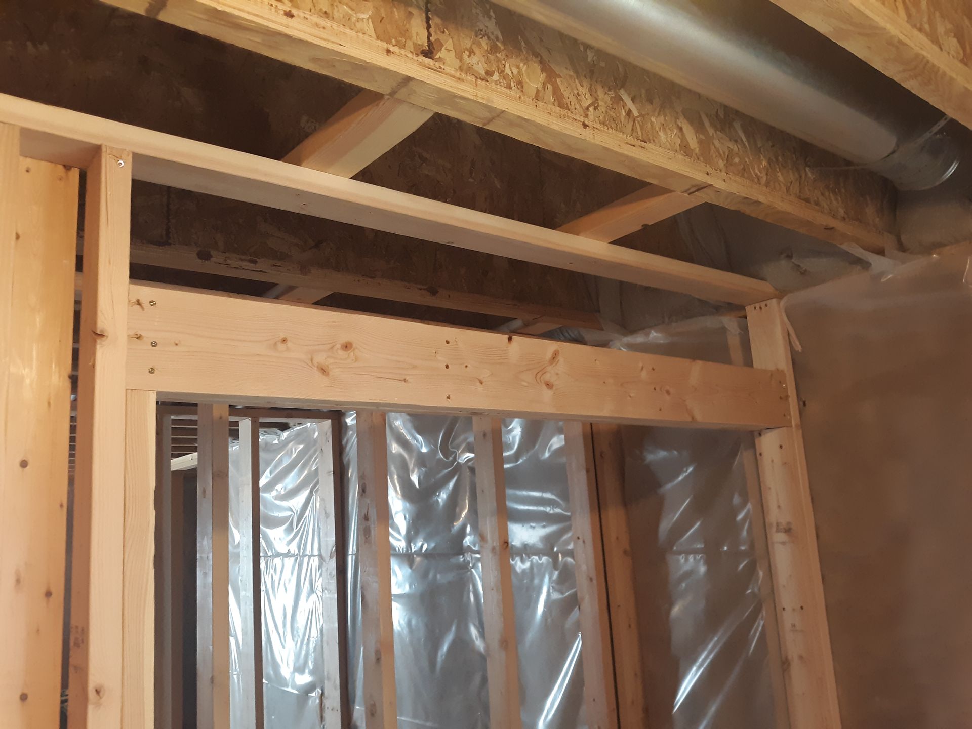 Framing of a doorway in a new construction basement with plastic sheeting and ductwork overhead.