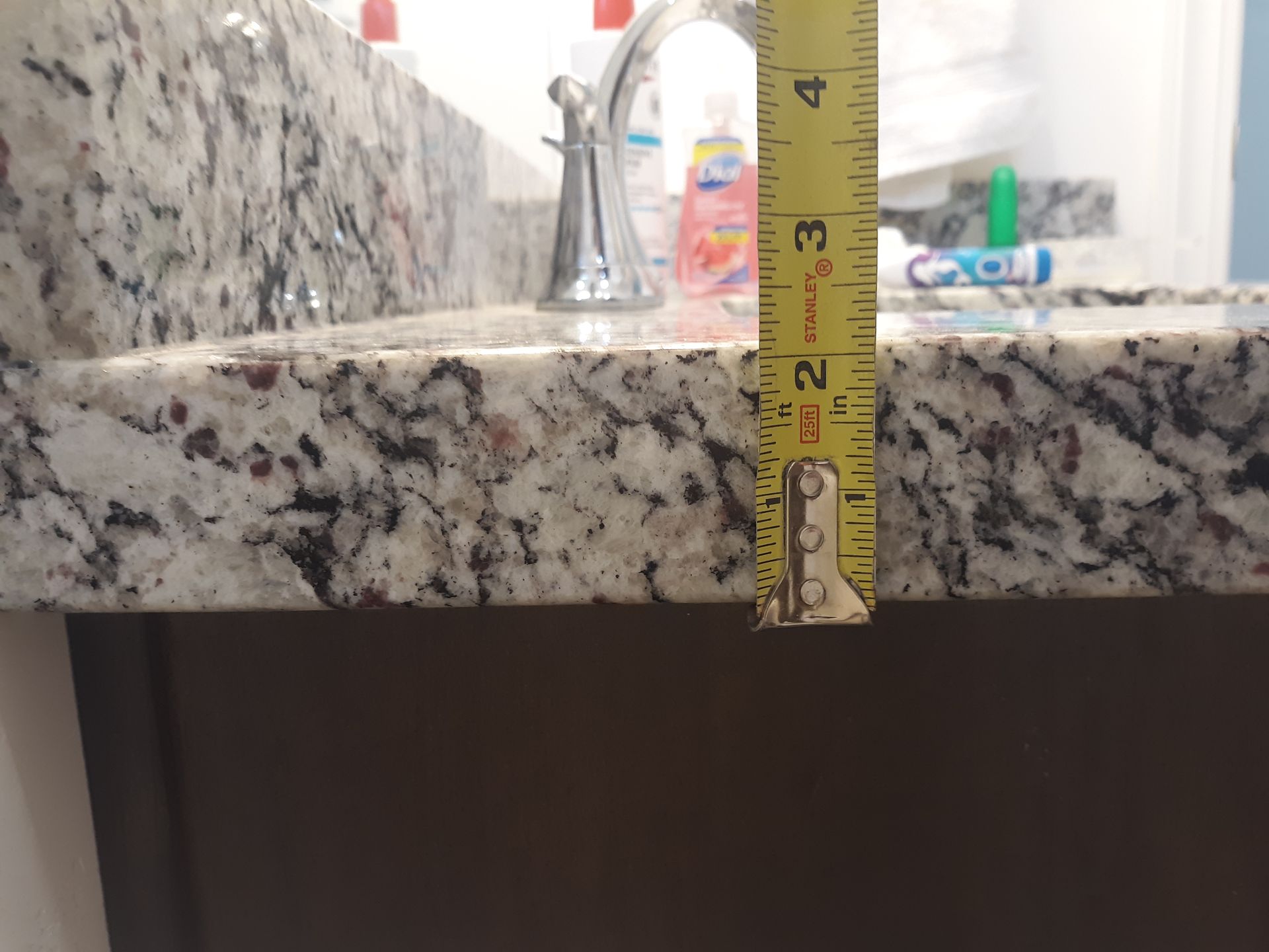 Tape measure shows a granite countertop is about 2 inches thick, above a brown cabinet.
