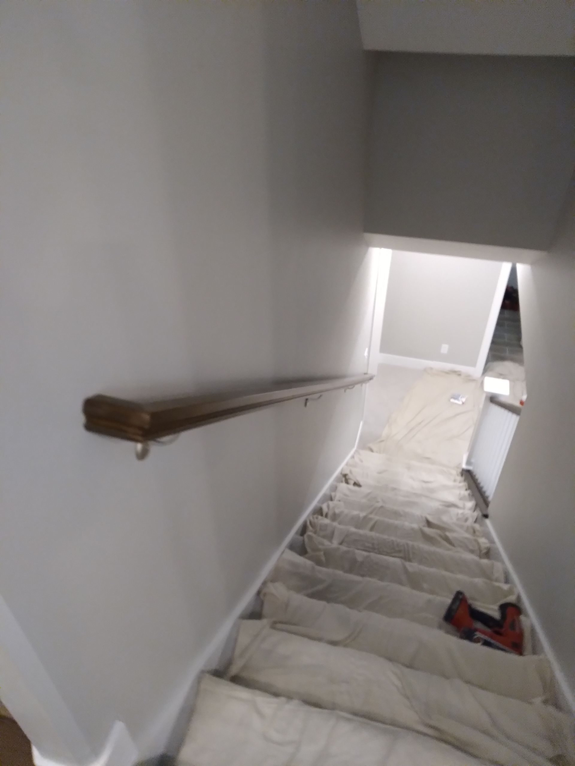 Staircase leading downwards, with a wooden handrail. The stairs are covered in white protective sheeting.