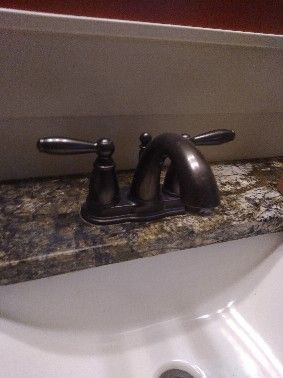 Bronze faucet with two handles on a speckled countertop above a white sink.