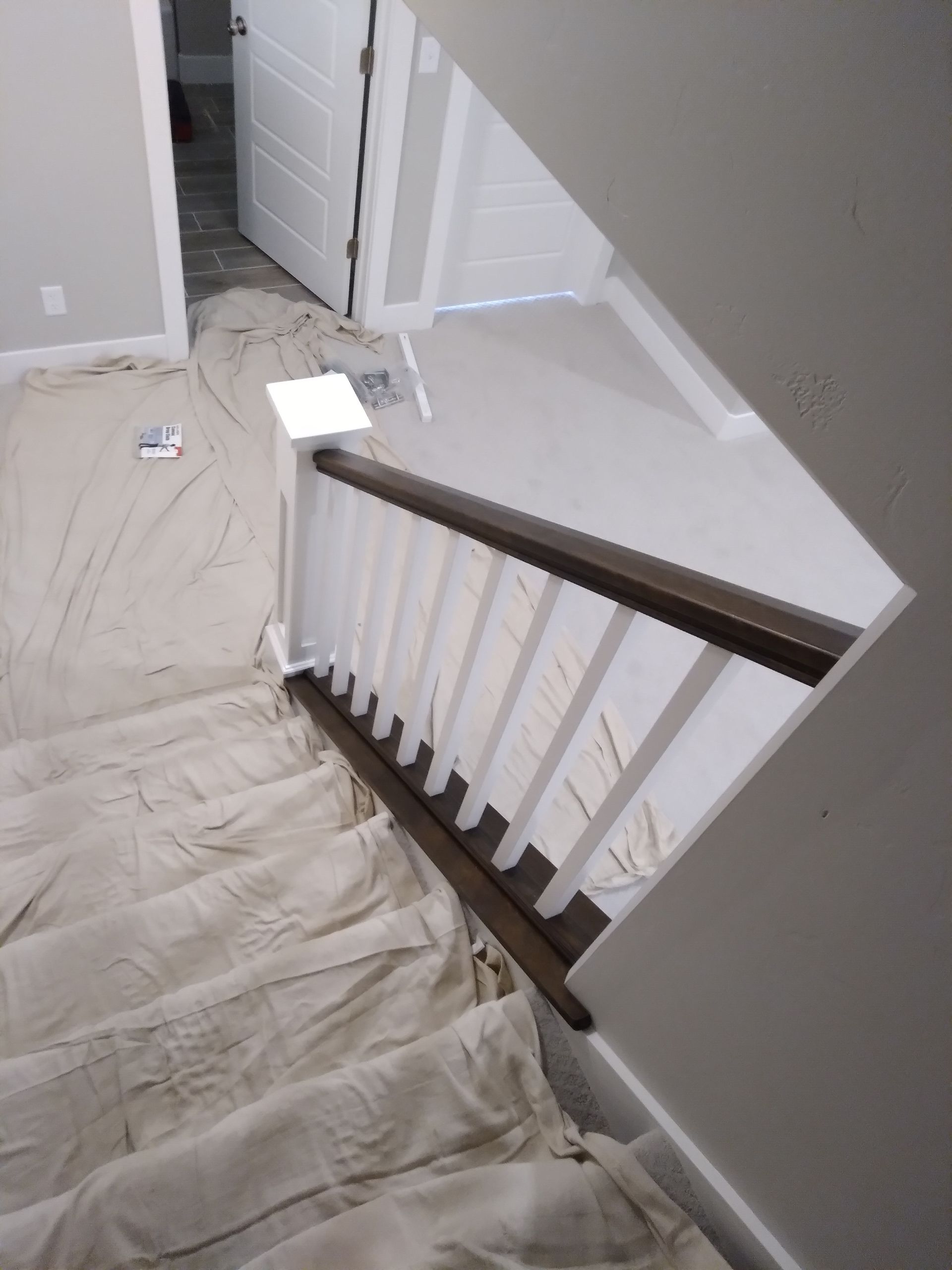 Staircase with white railing, brown handrail, and cloth covering the steps.
