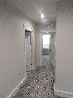 Hallway with carpet, beige walls, and doorways leading to rooms with windows.