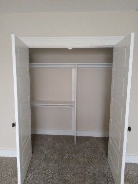 Open white closet doors reveal an empty closet with shelves and a clothes rod. Beige walls and carpet.