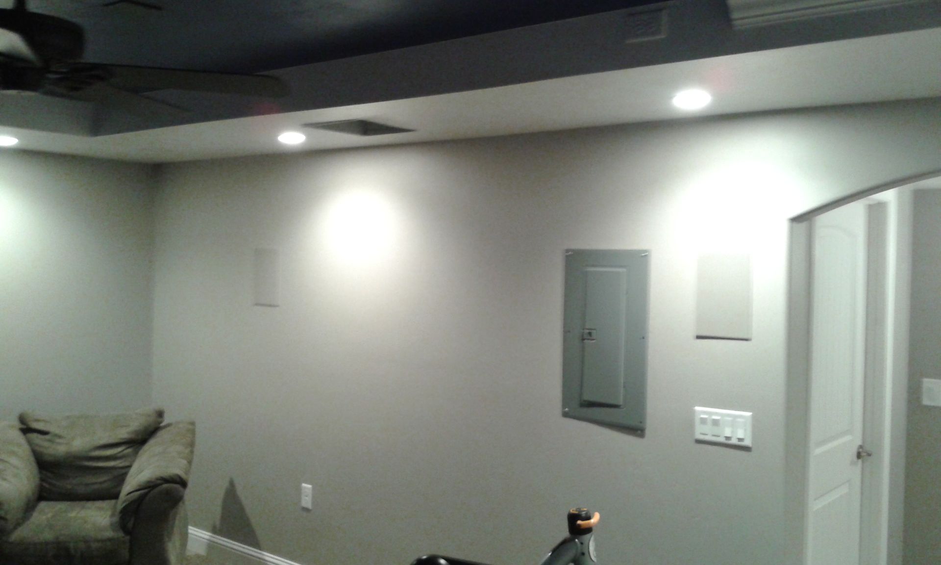 Gray-walled room with recessed lights, electrical panel, and an arched doorway. A comfy chair is visible on the left.