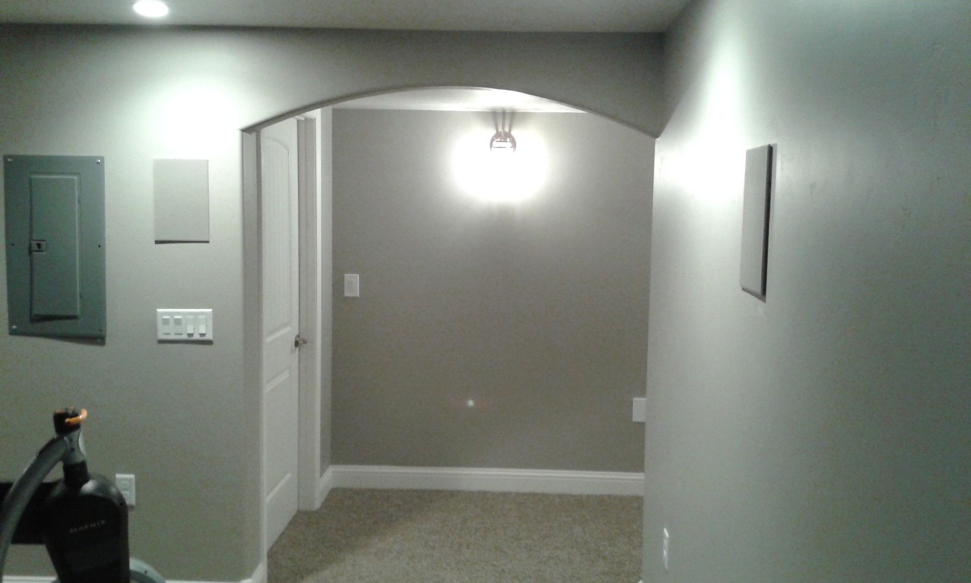 Gray-walled hallway with an arched doorway, white door, and recessed lighting. A circuit box is visible on the left.