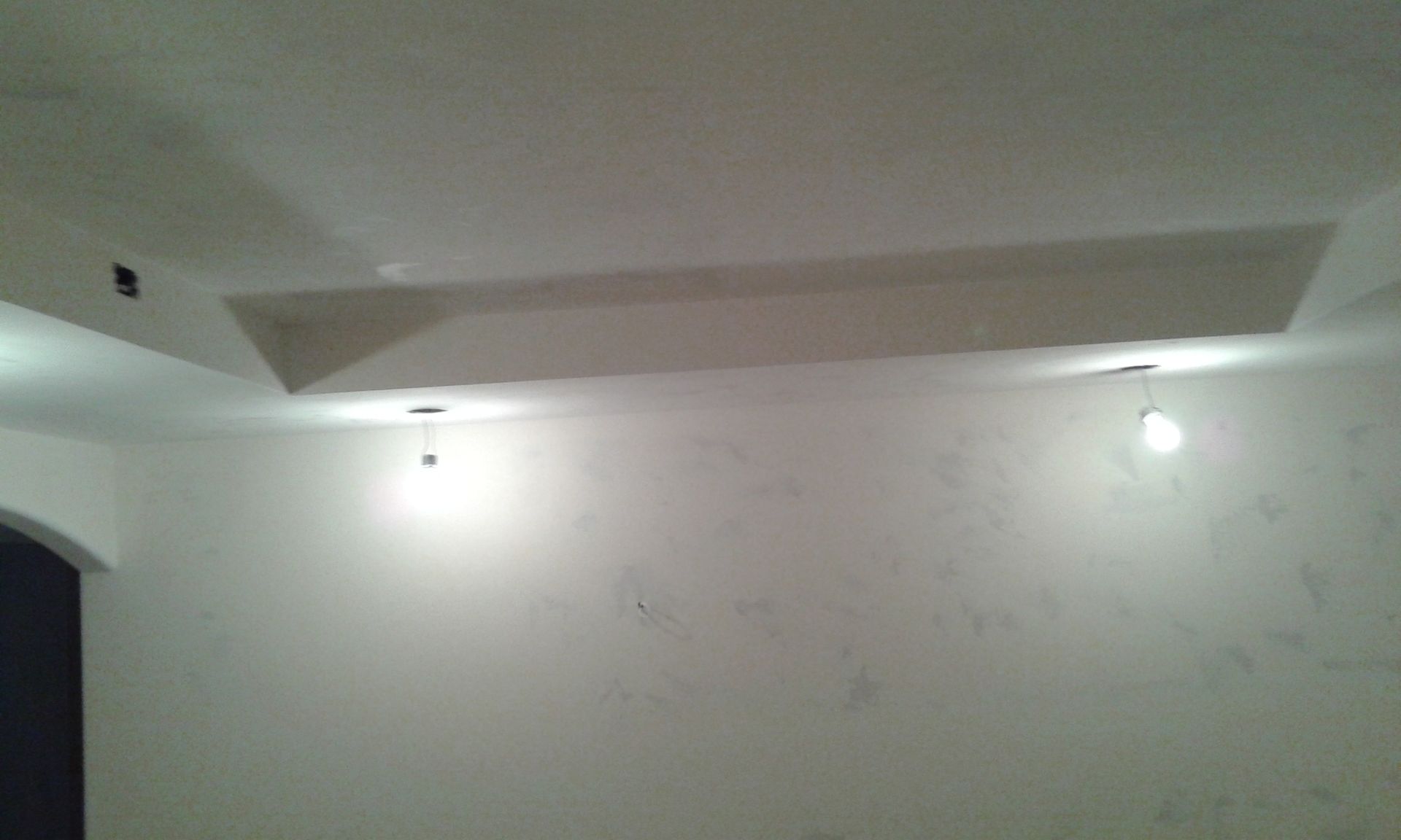 White room with recessed ceiling and two hanging lightbulbs.