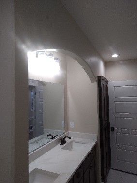 Bathroom with vanity, mirror, arched ceiling detail, and dark brown storage cabinet.