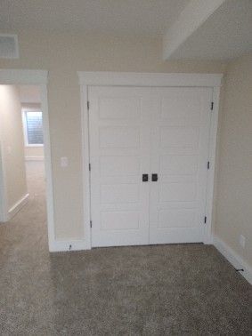 White closet doors in a room with beige walls and carpet. A doorway is visible on the left.