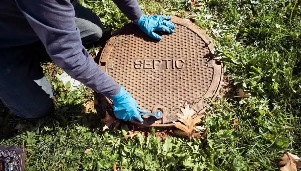 Worker opening a round utility manhole cover in grass with blue gloves and tools