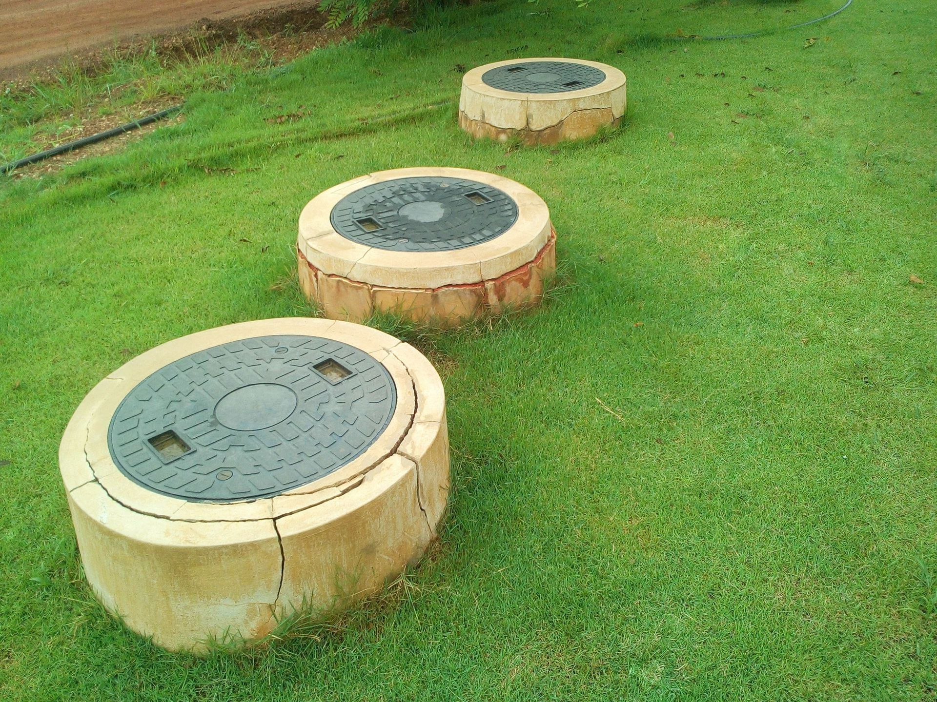 Three circular concrete utility covers on a grassy lawn near a path