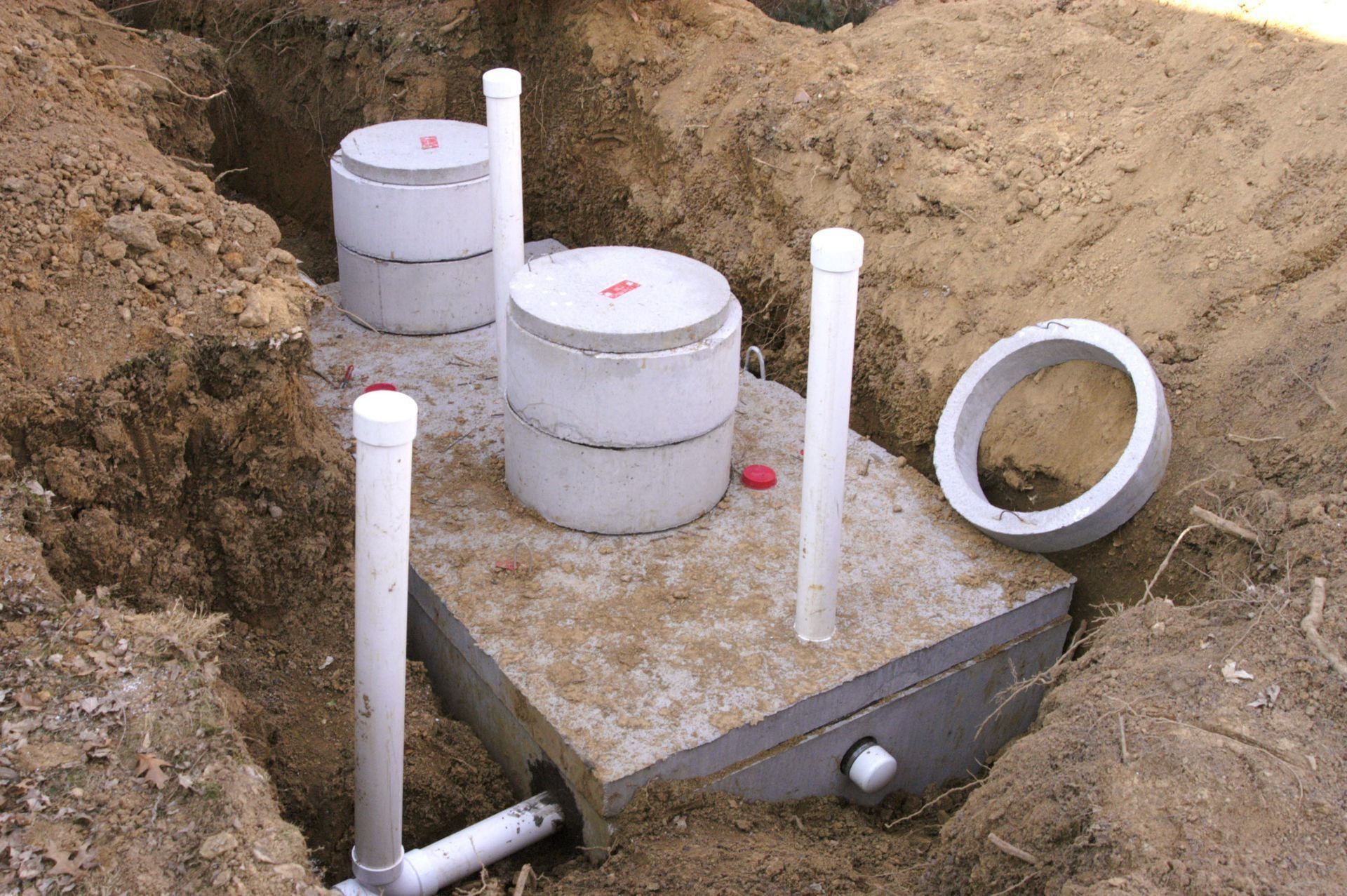 A septic system being installed in a trench. Includes concrete tanks, piping, and access covers, surrounded by dirt.