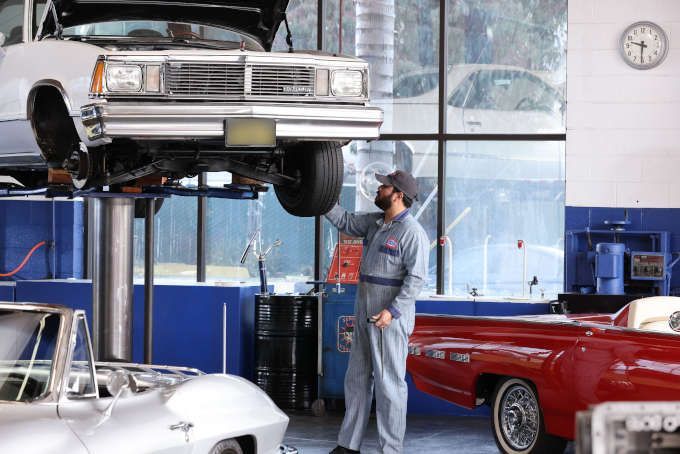Mechanic inspecting a car on a lift in an auto repair shop, with red and silver cars nearby