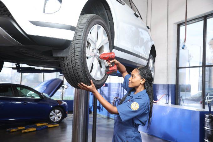 Mechanic using a red impact wrench to repair a white SUV in an auto shop