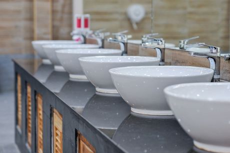 Row of white ceramic sinks on a dark countertop in a tiled restroom