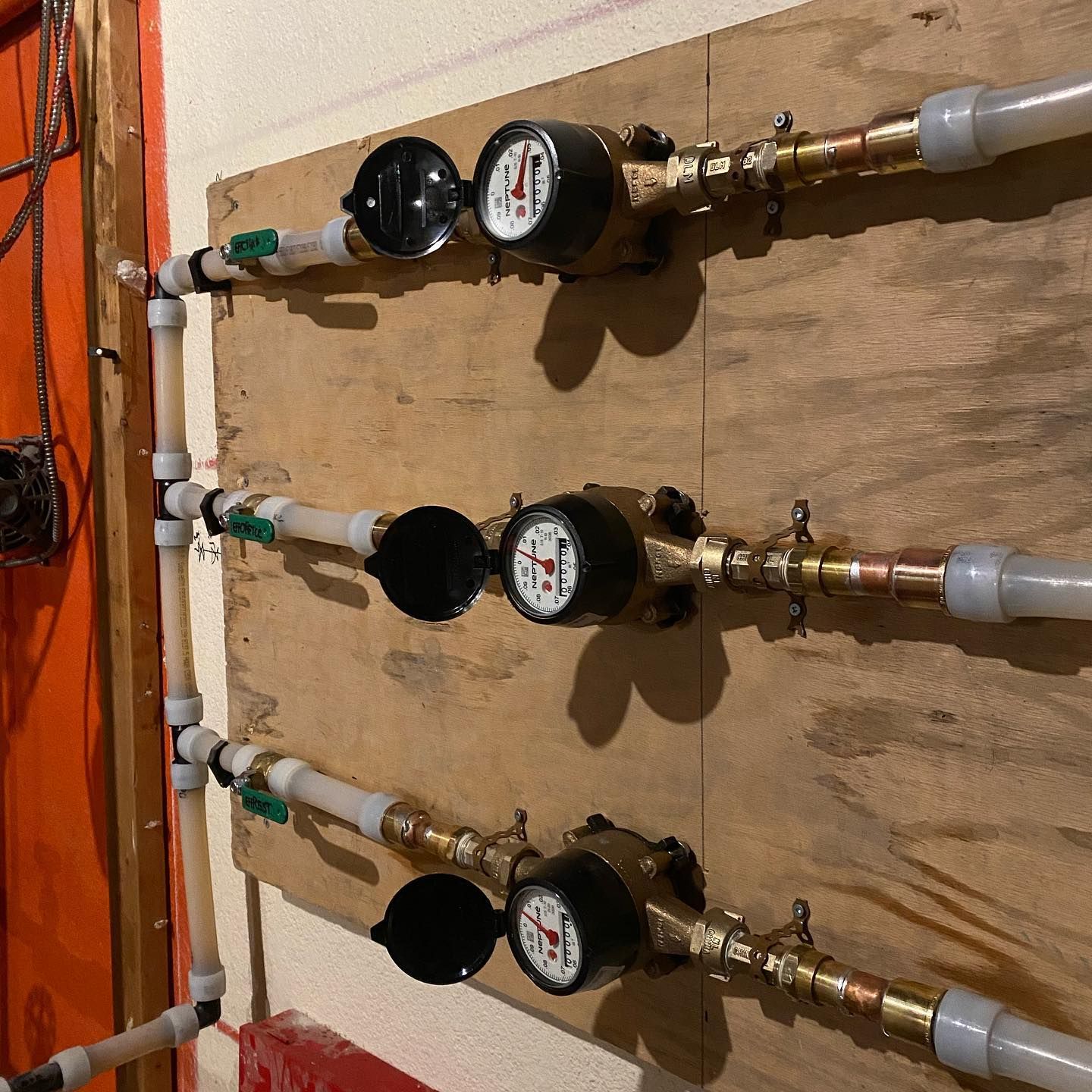 Three water meters and pipes mounted on a wall, with orange paint and beige insulation.