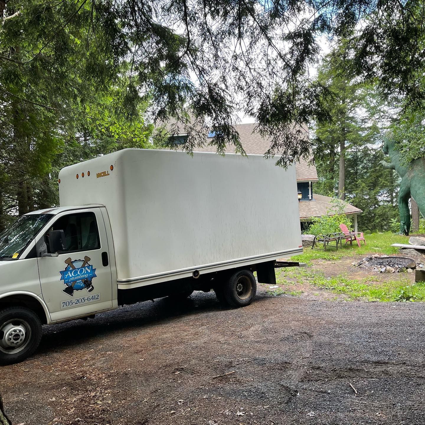 White box truck parked on a gravel driveway under trees near a house