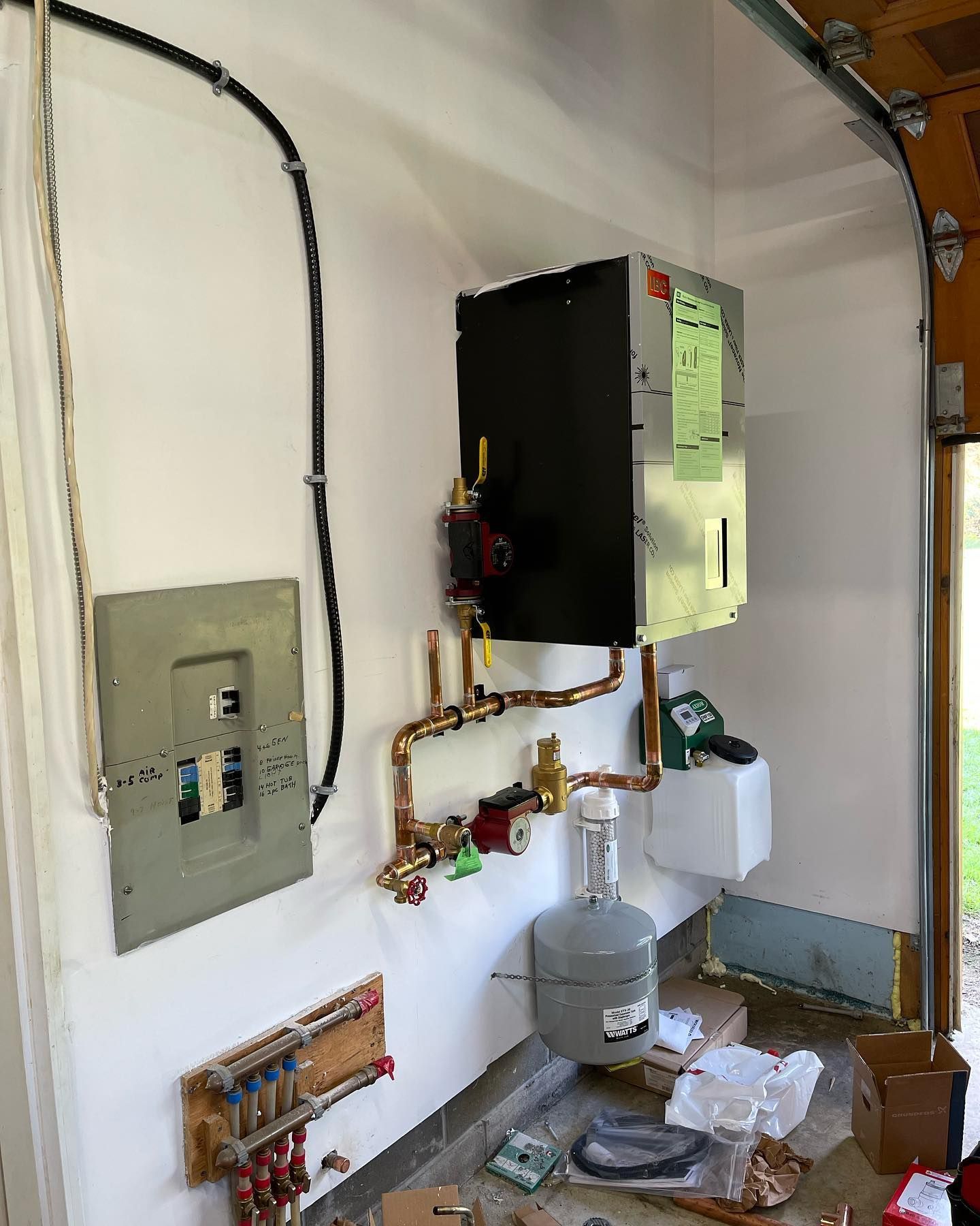 Wall-mounted boiler and control panel with copper pipes in a utility room, with tools on the floor.