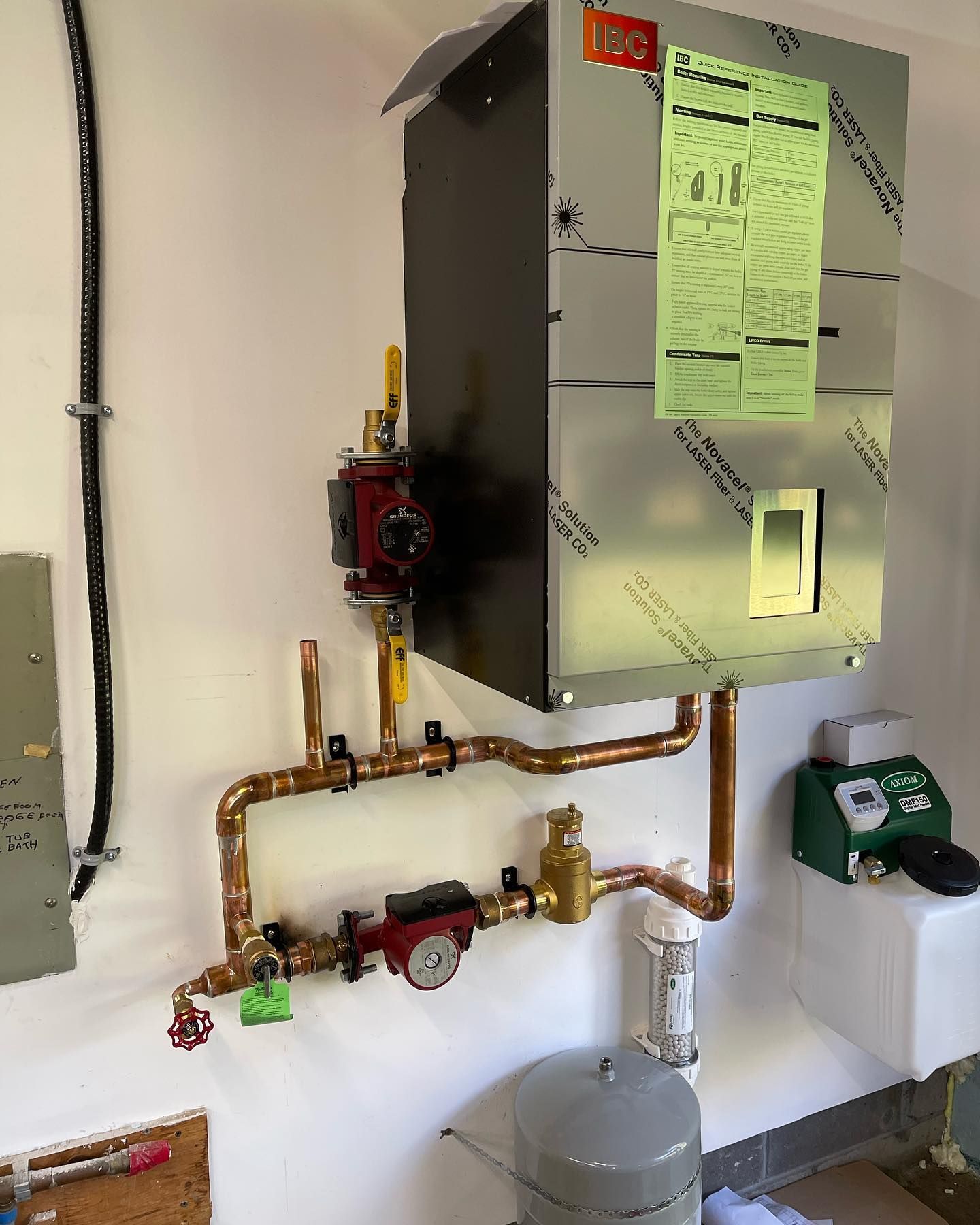 Wall-mounted boiler with copper pipes, gauges, and a green inspection sheet in a utility room