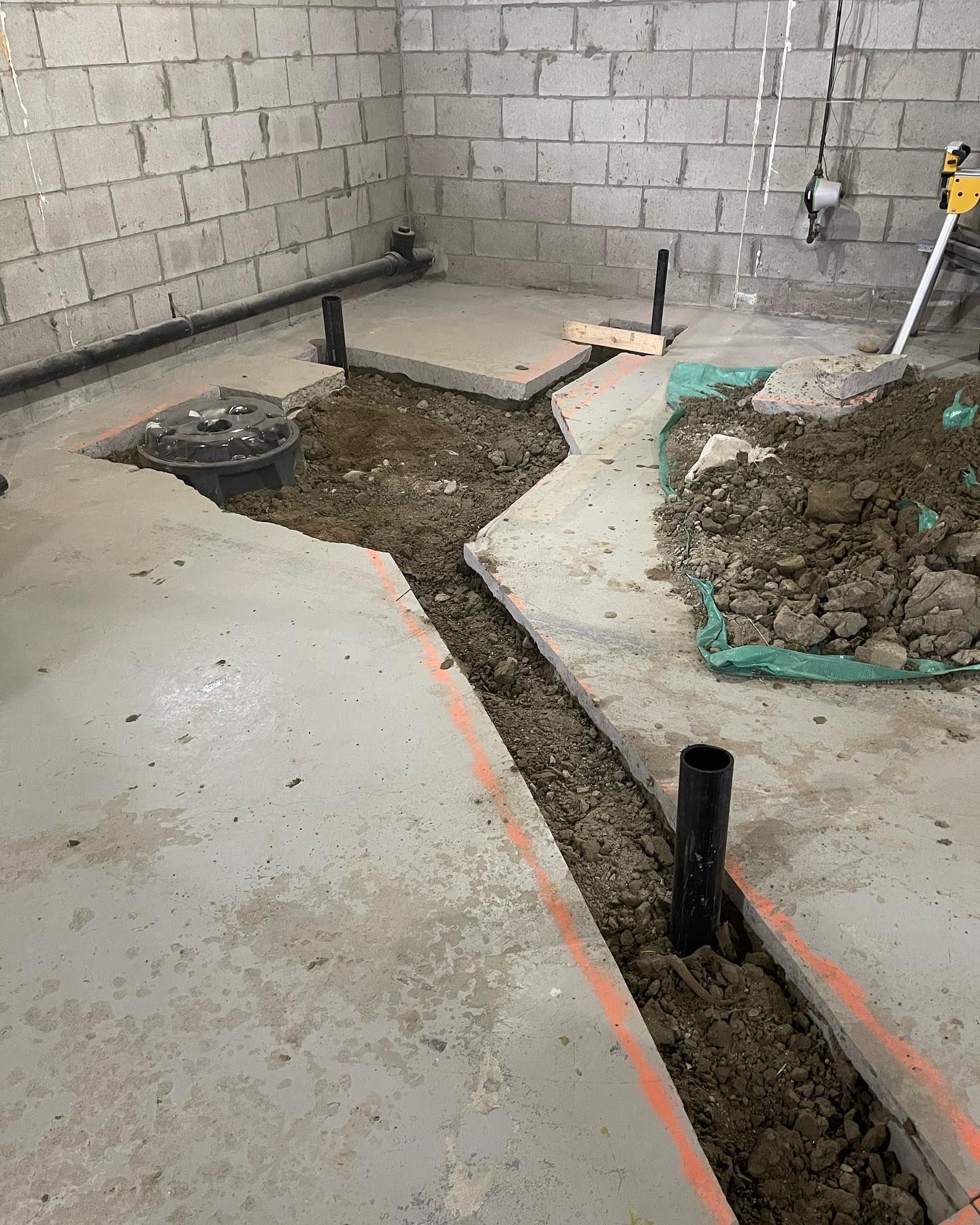 Construction floor with trenches and exposed pipes inside unfinished concrete room