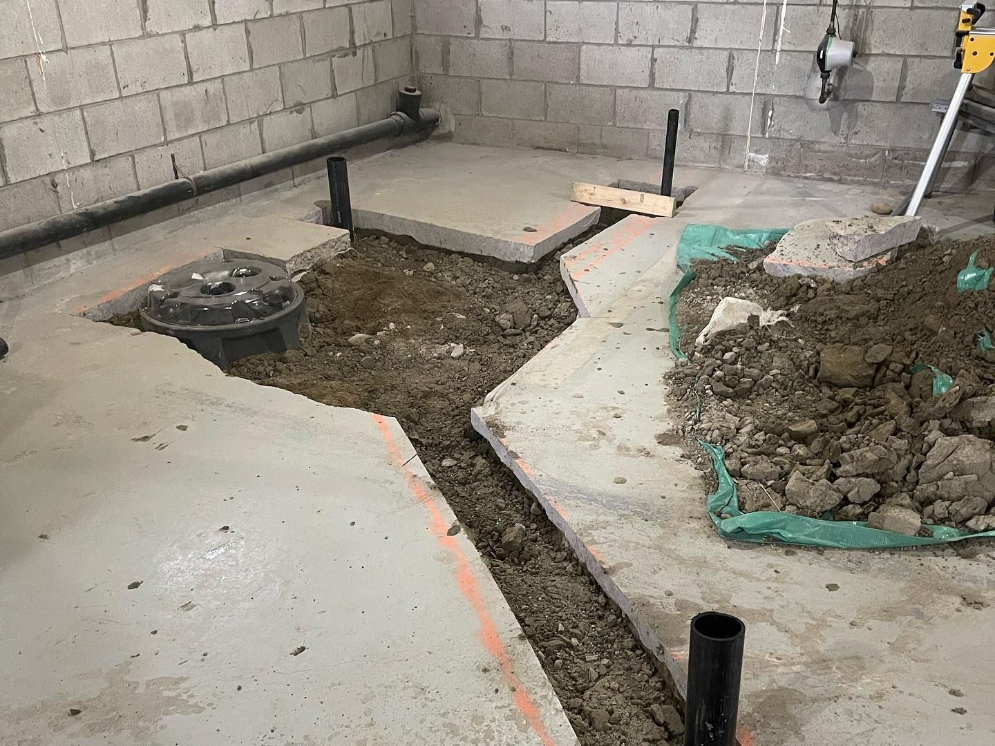 Partially dug concrete floor in a basement with exposed soil, cinderblock walls, and piled dirt