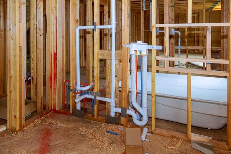 Partially built bathroom framing with exposed plumbing pipes and a white bathtub
