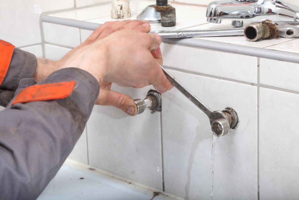 Hand turning a chrome faucet handle on a white tiled sink wall