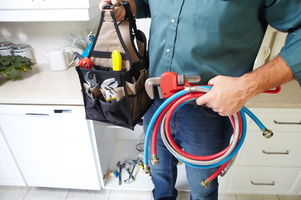 Plumber holding coiled red and blue hoses beside a sink in a kitchen area