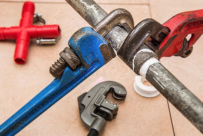 Assorted pipe wrenches and fittings on a tiled surface, including blue, red, and gray tools.
