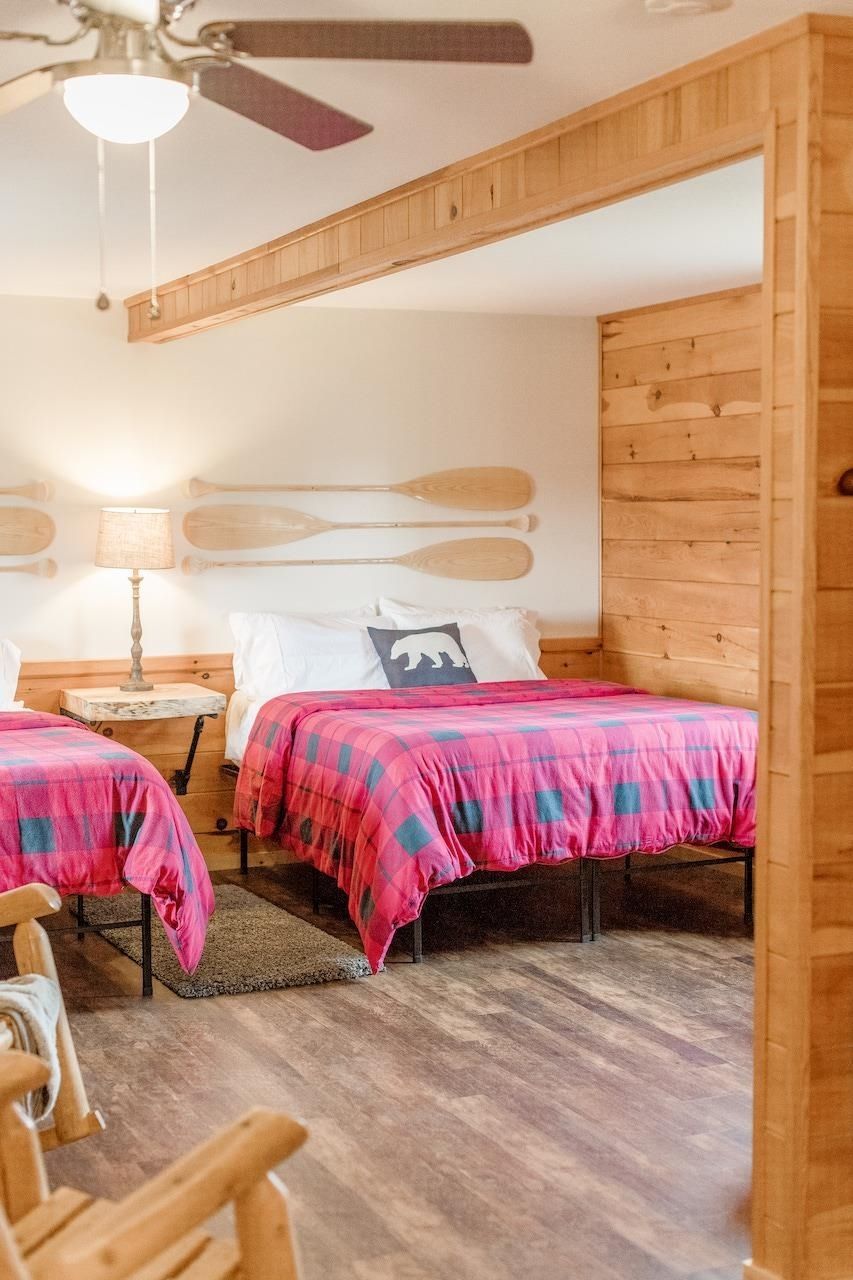 Rustic bedroom with two twin beds, pink bedspreads, wooden decor, and a ceiling fan