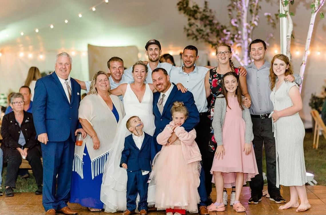 Group of people posing indoors at a celebration, with a child in a pink dress at the front.