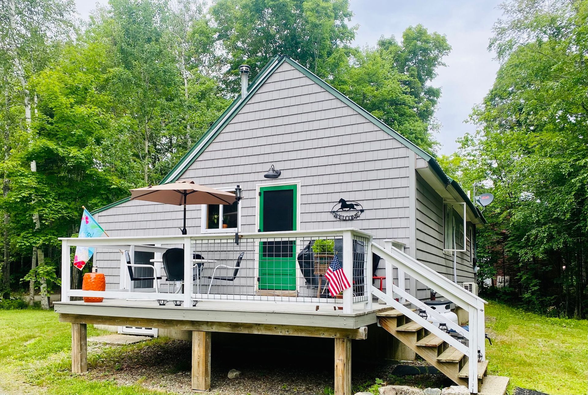 Gray cabin with green door and porch on stilts surrounded by trees