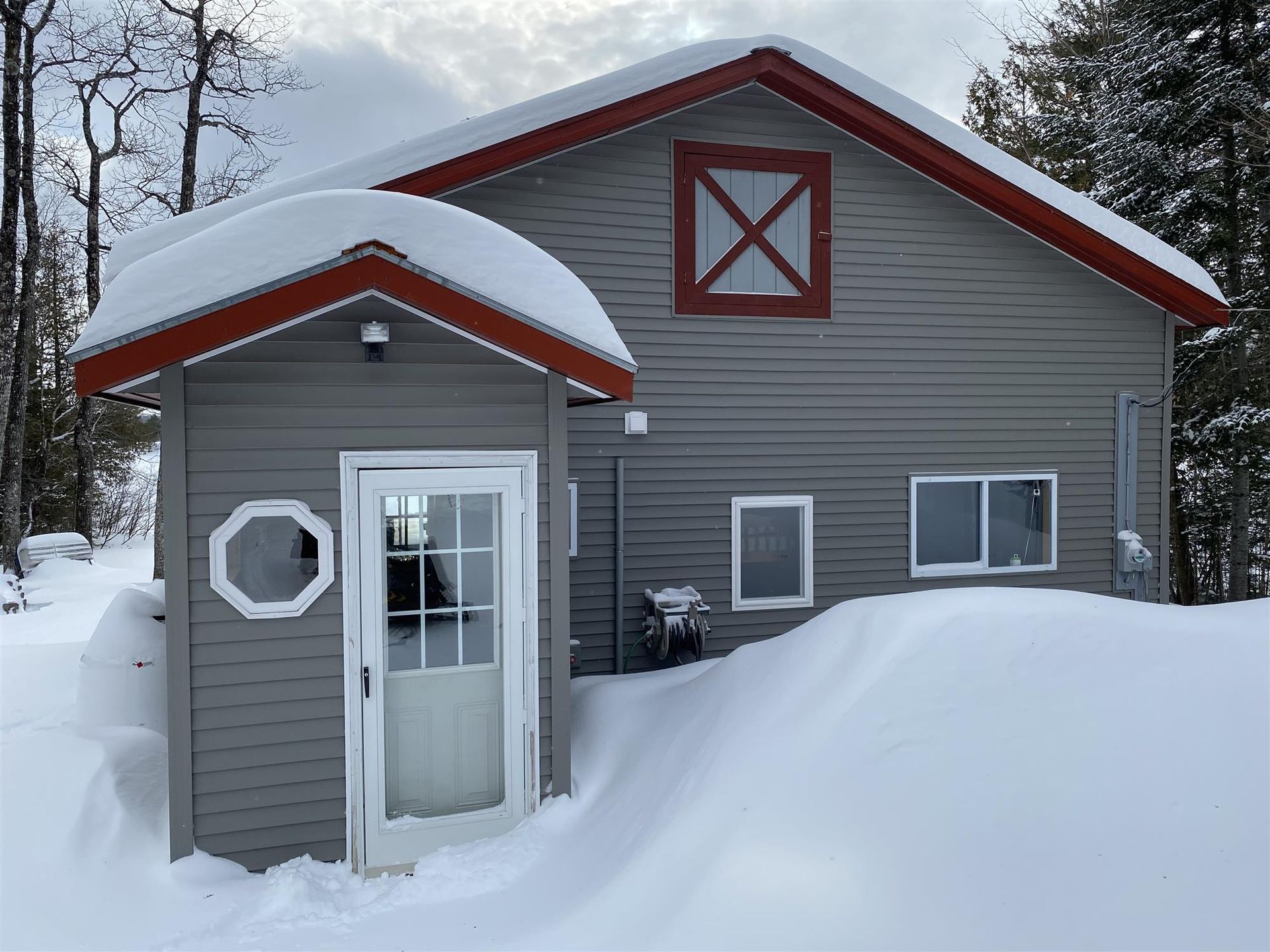 Snow-covered gray house with red trim and a small front entry in winter