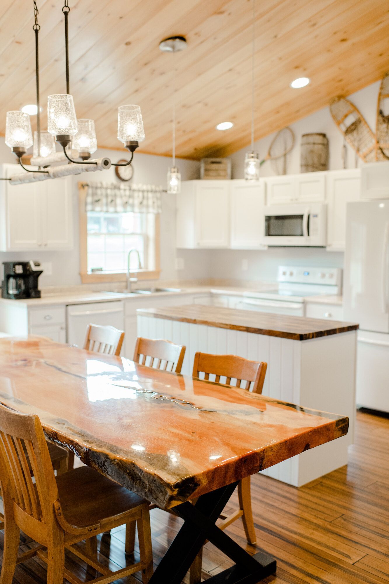 Bright kitchen with white cabinets, wood ceiling, island, and rustic wooden dining table