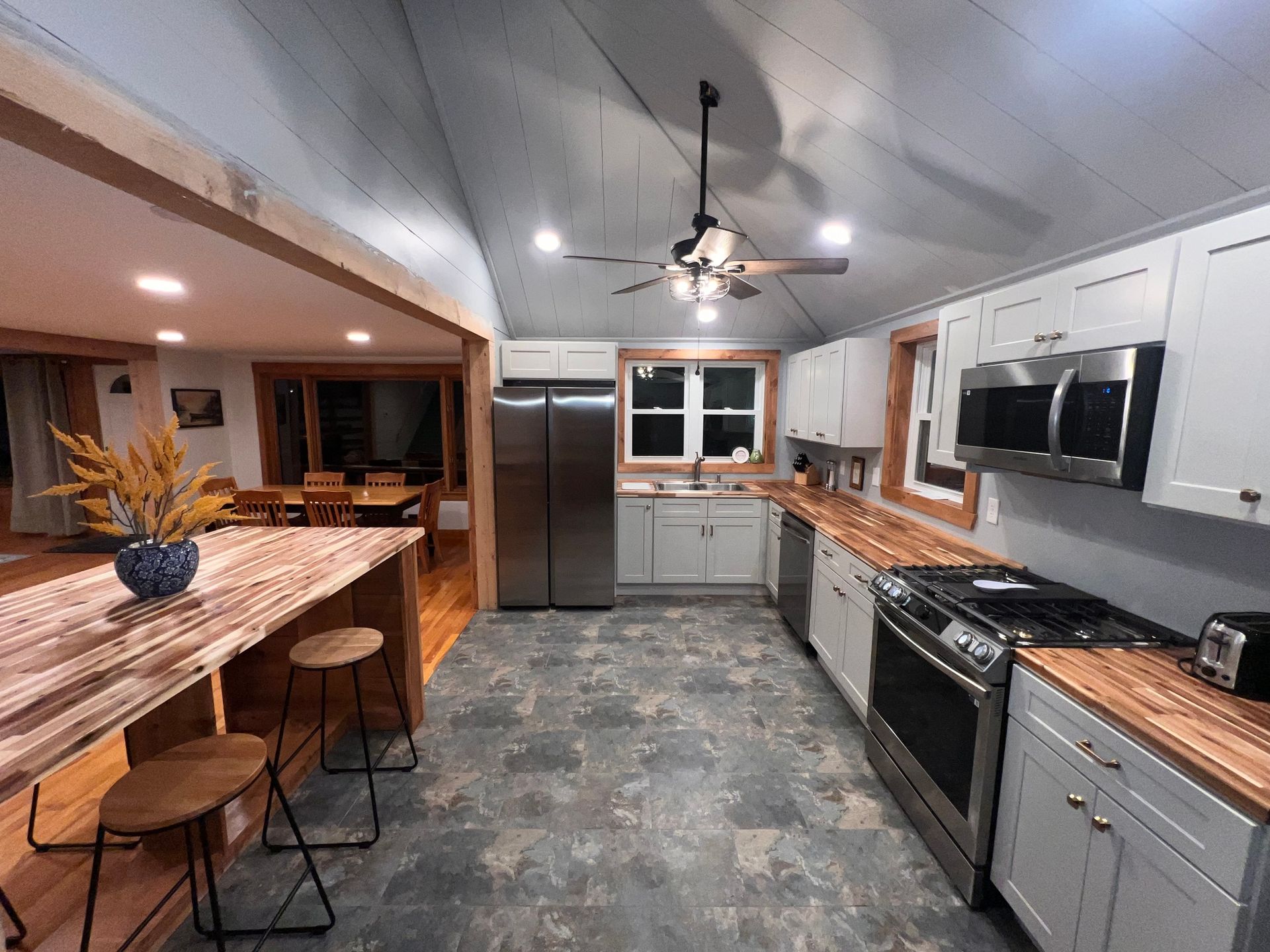 Modern kitchen with gray cabinets, stainless appliances, wood island, and ceiling fan